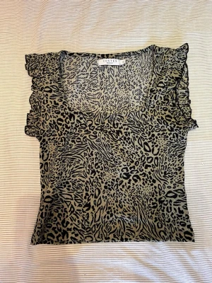 Leopardmönstrad topp  - Snygg leopardmönstrad topp från Costes i beige och svart. Toppen har volangdetaljer vid axlarna.