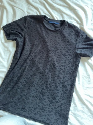 Svart  t-shirt med mönster - Snygg svart t-shirt  med diskret mönster över hela plagget. Tillverkad i 100% bomull och har en klassisk rund halsringning och korta ärmar. Perfekt för dig som vill ha en stilren men ändå unik look.