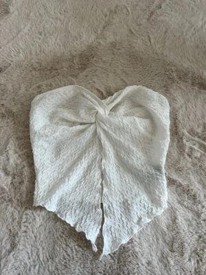 Vit  bandeau tubtopp - Säljer en vit bandeau tubtopp i spets med omlottliknande twist framtill. Prefekt till sommaren som topp eller som cover up. Aldrig använd, storlek XS