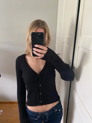 Svart ribbad kofta från Vero Moda - Säljer en svart ribbad kofta från Vero Moda med v-ringning och knäppning framtill. 