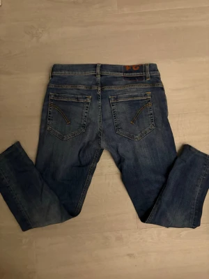 Blå Dondup jeans med slitningar - Säljer ett par blå jeans med lätt slitna detaljer och klassisk femficksdesign. Jeansen har raka ben och kontrastsömmar på bakfickorna. Perfekta för en avslappnad och trendig look.