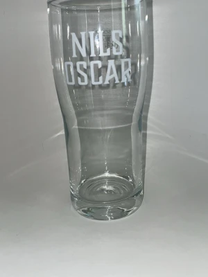 Nils Oscar ölglas - Säljer ett stilrent ölglas från Nils Oscar med vit logotyp på framsidan. Glaset är transparent och har en klassisk, avlång form som passar perfekt för att servera öl. Materialet är tåligt glas och designen är enkel men snygg.