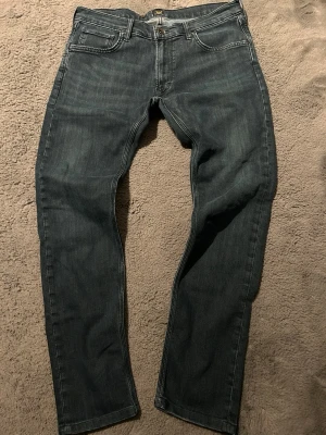 Mörkblå raka jeans från Lee - Snygga jeans från Lee med klassisk femficksdesign och raka ben. Jeansen har Lee-logga på bakfickan och patch i midjan. Tillverkade i slitstarkt denimtyg som passar perfekt till en avslappnad stil. Tyvärr är lapp för storlek bort klippt så storlek är okänd. Men uppskattar ca w30 SE MÅTT!
