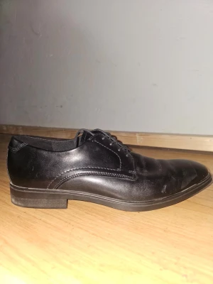 Svarta loafers i skinn från Ecco - Pris kan diskuteras. Säljer ett par klassiska svarta loafers från Ecco i äkta skinn. Skorna har rundad tå, diskreta sömmar och svart snörning. Sulan är i slitstark gummi med Ecco-logga på insidan. Perfekta för dig som gillar stilrena och bekväma skor. Använt tre gånger, då jag inte passade i dem helt. 