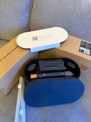 Dyson Airwrap Complete hårstyler - Säljer en Dyson Airwrap Complete hårstyler med flera tillbehör i en snygg mörkblå förvaringsväska. Perfekt för att skapa lockar, volym eller släta frisyrer. Kommer med olika borsthuvuden och stylingverktyg. Allt är original från Dyson.