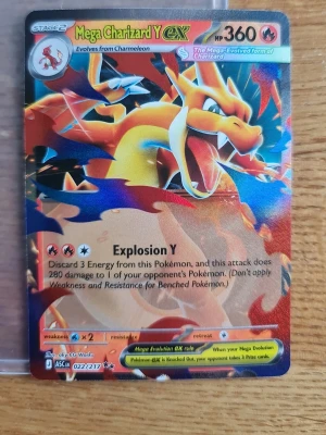 Mega Charizard Y EX Pokémonkort - Säljer ett Mega Charizard Y EX samlarkort från Pokémon. Kortet har färgstark design med Charizard i eldig pose och detaljer i rött, gult och blått. Kortet är gjort av laminerad kartong och har holografiska effekter. Perfekt för samlare eller Pokémonfans.