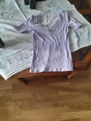 Ljuslila ribbad topp med spets - Supersöt ljuslila topp med ribbad struktur och v-ringning dekorerad med spetsdetaljer. Kortärmad och figurnära passform, perfekt för att lyfta vilken outfit som helst.