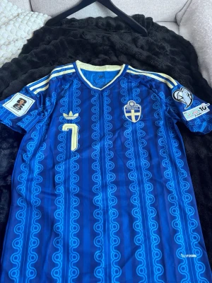 Sverige VM 2026 Bortaställ Bergvall #7 - Säljer en blå matchtröja från Sverige med nummer 7 och namnet Bergvall på ryggen. Tröjan har gula detaljer, officiella landslagsmärket, Adidas-logga och tryck på båda ärmarna. Tillverkad i lätt och ventilerande material.