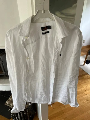 Vit linneskjorta från Morris - Klassisk vit skjorta från Morris i svalt linne. Skjortan har lång ärm, knappar framtill och en liten broderad logga på bröstet. Perfekt för varma dagar och enkel att styla till olika looks. Passar perfekt till sommaren! Storlek Xs men passar S! Hör av er vid frågor! 