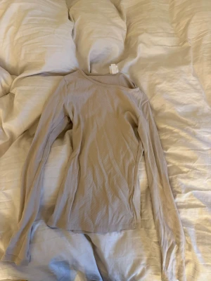 Beige ribbad långärmad topp - En stilren beige långärmad topp med ribbad struktur. Toppen har en rund halsringning och är figurnära i modellen, perfekt att styla till jeans eller kjol. Enkel och snygg bas i garderoben.