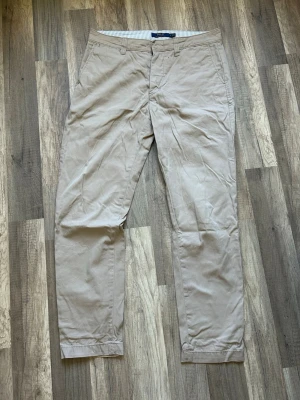 Beige chinos från Polo Ralph Lauren - Snygga beige chinos från Polo Ralph Lauren med klassisk rak passform. Byxorna har sidofickor, två bakfickor med knapp och diskret logga broderad ovanför ena bakfickan. Tillverkade i mjuk bomull för en bekväm känsla.