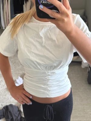Vit croppad topp med rynkdetalj - Säljer en vit croppad topp från cider i strl XS med korta ärmar och snygg rynkdetalj i midjan. Perfekt till jeans eller kjol för en trendig look.