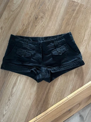 Svarta shorts med fickor - Snygga svarta shorts med två framfickor med lock och knappdetaljer. Lågmidjade.
