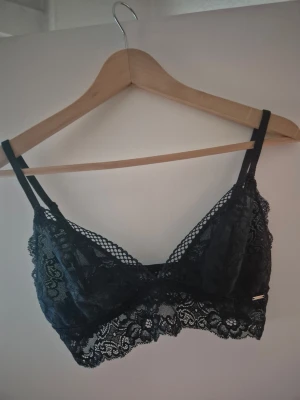 Svart spets-bh från ELLA M Mörkblå, fint skick  - Snygg svart bh från ELLA M i storlek M. Bh:n är tillverkad i mjuk spets med blommigt mönster och har tunna axelband. Modellen är utan bygel och har dekorativ kant nertill. Perfekt för dig som gillar en feminin och bekväm stil.