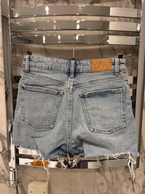 Ljusa denimshorts - Säljer ett par ljusblå denimshorts med slitna detaljer framtill och klassiska fem fickor. Perfekta för en avslappnad och trendig look. 