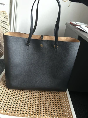 Svart väska från Ralph Lauren - Stilren svart väska från Ralph Lauren Väskan har en enkel, rymlig design med öppen topp och en stor ytterficka på baksidan. Inga slitage!
