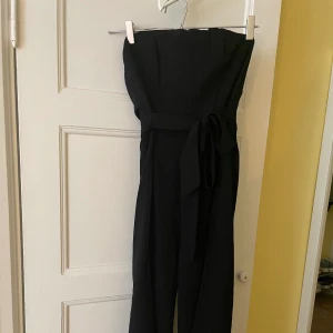 Strapless Svart Jumpsuit från Princess Polly - Svårt att få den bra på bild men jätte bra bas bandeau svart jumpsuit! Den har ett band i midjan som man kan knyta i rosett där bak eller fram! Aldrig använt :) 