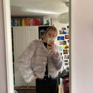Pälsjacka (fake päls) - Köpt för 900 kr från madlady. Väldigt fin ljus lila-grå pälsjacka (ej äkta päls). Använd max 5 ggr, säljes pga inte min stil längre. Lappen finns kvar. Har knappar så går att stänga, knapparna är gömda i pälsen så väldigt fint. Bra kvalité. Kan inte lägga upp fler bilder så skicka meddelande för mer :)