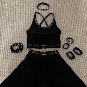 En disco-slow tävlingsdräkt i svart sammetstyg. Består av en topp med spännen på baksidan, en löst sittande kjol, fyra armband, en scrunchie och en choker (med spänne). Endast använd ett fåtal gånger och i bra skick. 