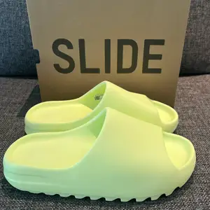 Yeezy slide glow green. Helt oanvända, storlek 44 1/2. Små i storleken, passar till dem som har 42 - 43. Köpta från Adidas Confirmed appen så kvitto mm finns. 