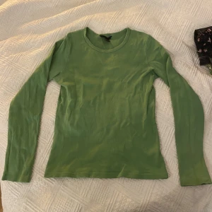Grön långärmad - Otroligt skön grön figursydd långärmad med ett gammalt material som tillägger en vintage touch. Storlek M med stretchigt material. Bild 3 visar färgen utan blixt. Rekommenderar!
