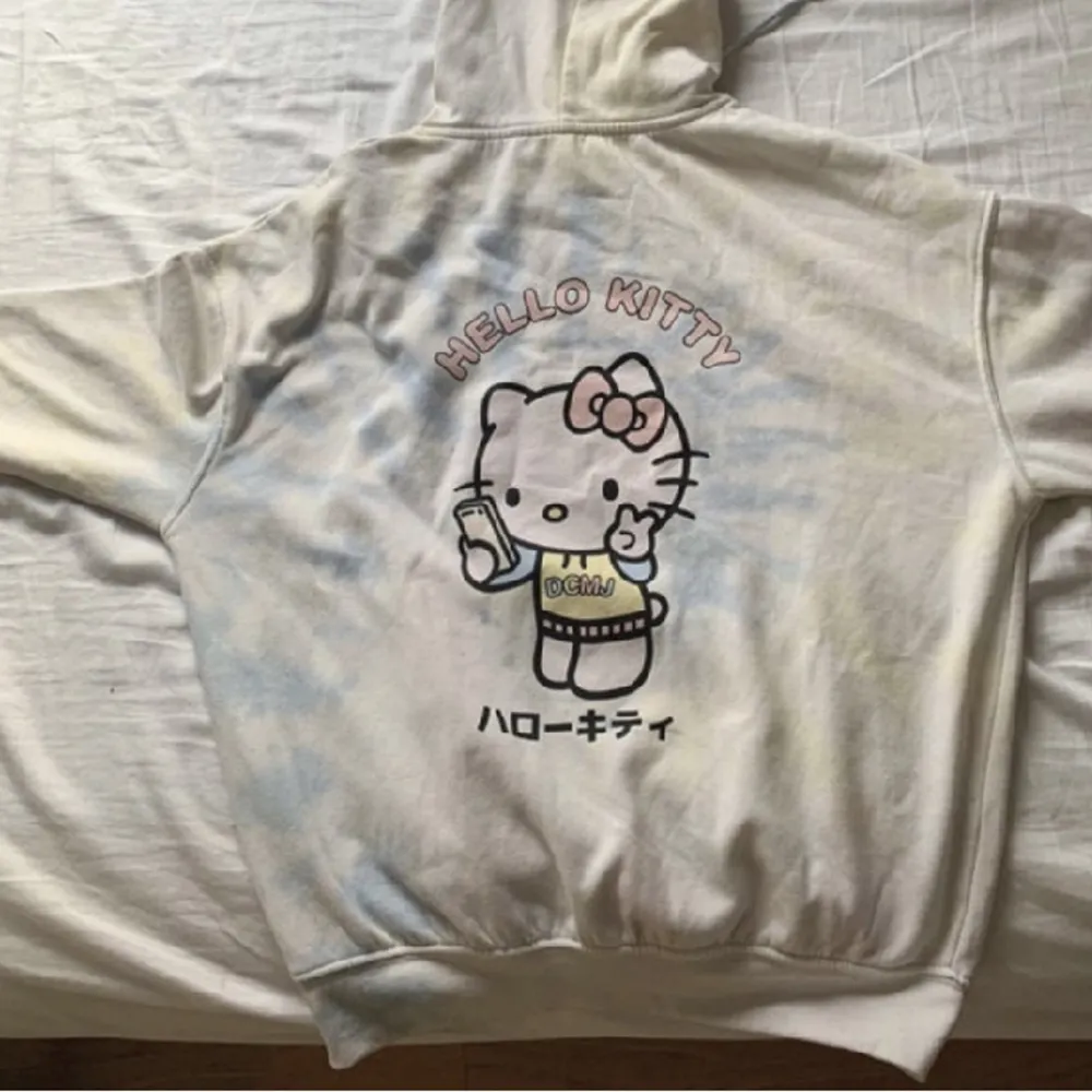 Hello Kitty, bra kvalitet, hoodie, grundfärgen är beige och så finns det lite blå, gul, vitt, rosa. Det finns Hello Kitty och japanska text på baksidan av tröjan.. Hoodies.