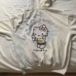Hello Kitty, bra kvalitet, hoodie, grundfärgen är beige och så finns det lite blå, gul, vitt, rosa. Det finns Hello Kitty och japanska text på baksidan av tröjan.