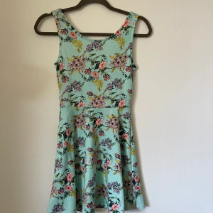 Klänning  - En turkos/ljusblå klänning med blommor på. Sparsamt använd men har vuxit ur den