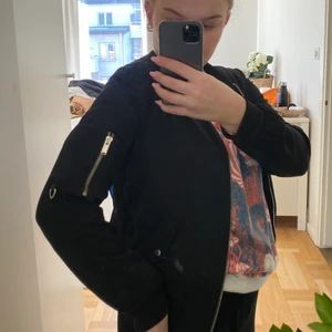 Svart bomberjacka - Snygg bomberjacka med silvriga detaljer på ena armen. Rätt tunnt tyg så passar till våren! Passar storlek 32-36 beroende på passform☺️