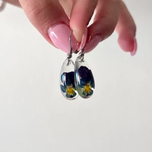 Örhängen  - Handgjorda örhängen med bevarad styvmorsviol 🌷avkok av blomman har förr används som behandling mot acne 🌞 örhänget är av allergivänligt kirurgisktstål 🧝🏻‍♀️✨spritar och gör rent smycket innan post 🍃