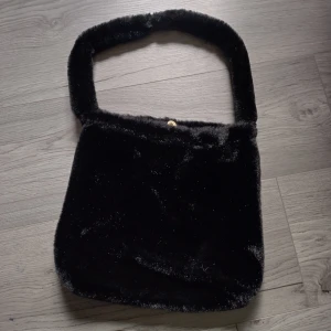 Väska - Fluffig svart axelväska. Den är i nyskick. Väskan är 28cm• 30cm och axelbandet är 63cm.