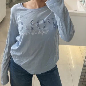 Ljusblå Ralph Lauren T-shirt  - Ljusblå långärmad Ralph Lauren T-shirt med tryck, knappt använt. Som storlek xs/s men är egentligen barnstorlek, storlek 170 (16 år)
