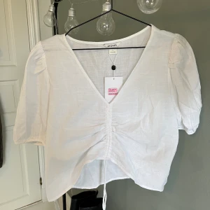 Blus - Vit blus från Monki med dragsko som man kan anpassa beroende på hur urringad och kort man vill ha blusen. Aldrig använd med prislappen kvar. Köparen står för frakten🫶🏼