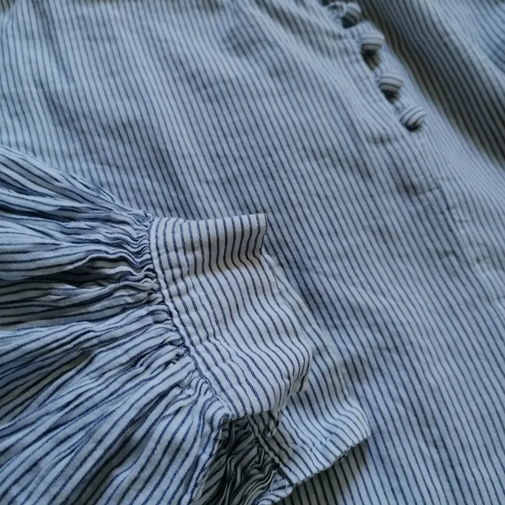 Cotton blouse with puffy sleeves, button closing and blue-grey stripes. Can be worn by someone who is between size S and XL. . Blusar.