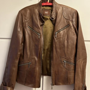 Skinnjacka från SAKI  - Så fin skinnjacka från saki, vintage. Sparsamt använd!!  Fin brun färg   Storlek 40, något liten i storleken