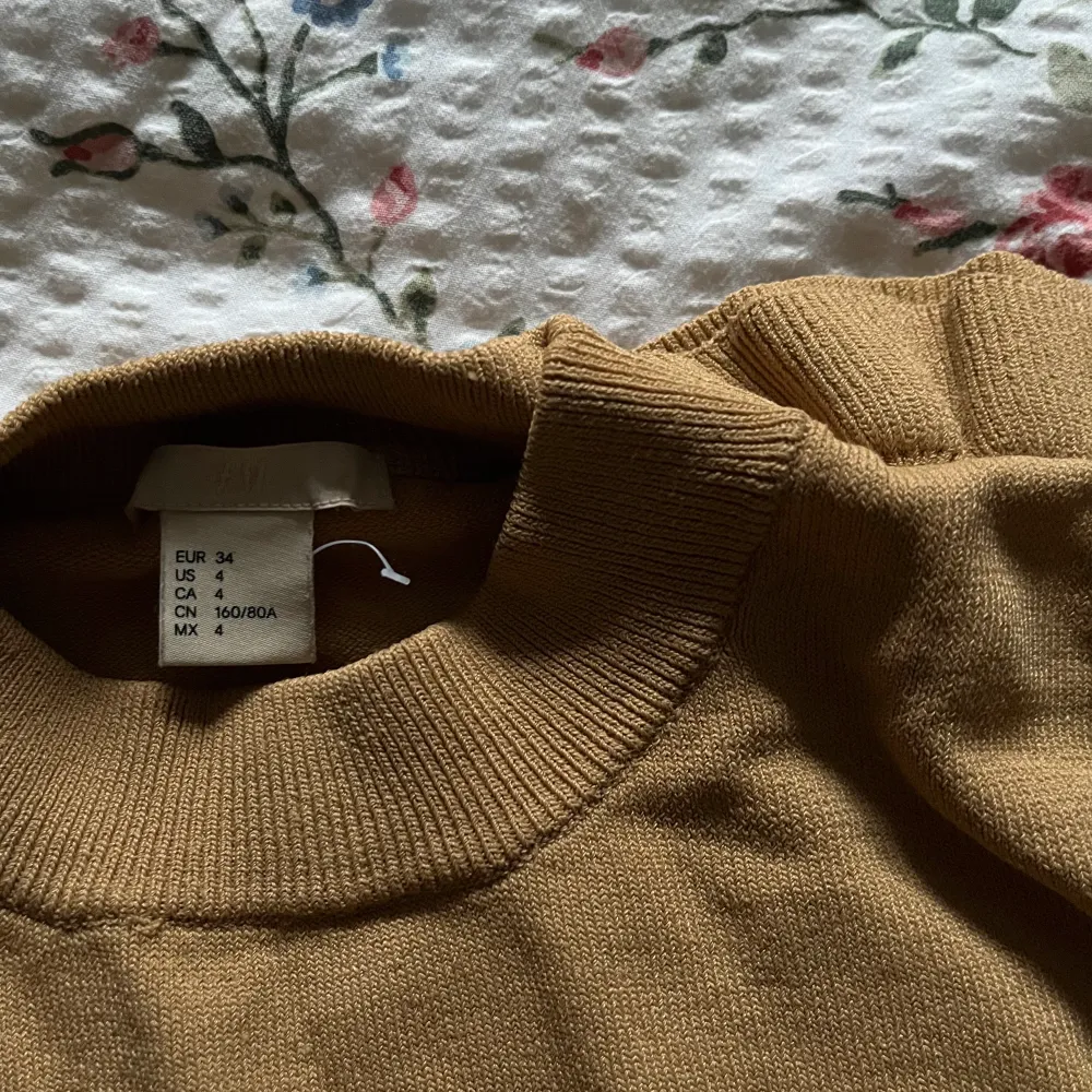 En finstickad mörkbeige tröja med populär volangdetalj från H&M. Helt i nyskick, utan defekter, i storlek 34. Frakt tillkommer💕. Stickat.