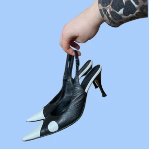 Svartvita klackskor - Svarta kittenheels med vita detaljer och öppen häl. Remmen som sitter runt hälen har ett spänne så man kan justera. Klacken är ca 8 cm.