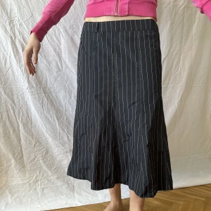 Randig knälång kjol - Svart kjol med vita ränder. Tjockt halv-glansigt material. Nästan oanvänd. 