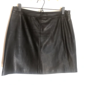 Svart fauxleather kjol - Svart fauxläder kjol från gina tricot. Nyskick. Storlek 40. Dragkedja vid sidan.