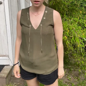 Militärgrönt linne med gulddetaljer  - Fint linne med detaljer i guld, strl M passar nog S också. Jag är 163cm lång 