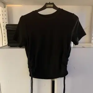 Oanvänd svart T-shirt från Zara. Har snören på båda sidor. Mjukt material! 