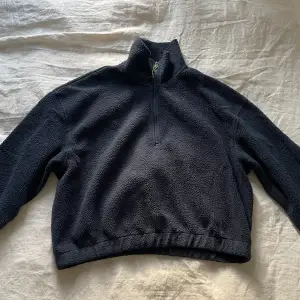 En mörkblå fleece, dragkedja med neongrön detalj. Lite croppad i modellen. Resor i slutet av ärmar och vid änden av tröjan.