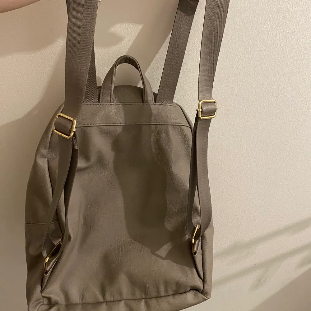 Säljer denhär gråa ryggsäcken från H&M. Väl använd men inga skador! Guldiga detaljer. . Väskor.