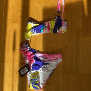 Baddräkt från Jaded Swim - Mönstrad baddräkt från Jaded Swim, köpt på asos, aldrig använd och både lapp + plastskydd kvar! En underdel som sitter ihop med överdelen med hjälp av en metallring, som även finns som detalj på överdelens Axel! Trosan sitter som en brazilian, och i övrigt ser den ut som en bikini bakifrån!