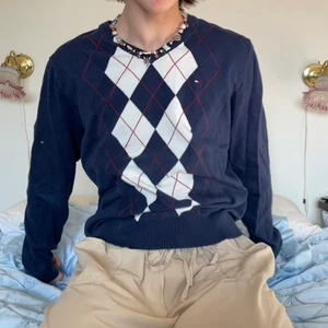 Mörkblå vit röd argyle rutig tröja Tommy - Mörkblå v-ringad Tommy Hilfiger tröja med vitt och rött rutigt argyle mönster samt broderad logga på bröstet 🦅  Så skön tröja med det härligaste mönstret för den som giller den mer preppy stilen! Släng på ett par kostymbyxor och par kängor och få en dark academia outfit! Passar perfekt nu till våren med en skjorta under eller till sommaren när det blir lite kallare om kvällen :)