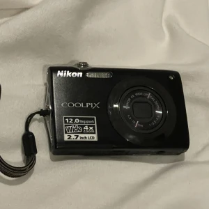 Nikon digitalkamera  - Nikon digitalkamera i super fint skick, inga repor eller andra skador! Är liten och tunn så den är perfekt att ta med sig överallt! Har blixt, timer, kan filma mm. Laddare, minneskort och fodral medföljer💗 