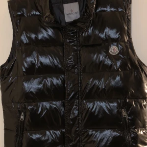 Monclerväst 2019 - Säljer nu min monclerväst som är köpt 2019, har inte kvar kvittot men man ni in verifiera den med qrkoden plus koden som står ovanför, den är autentisk. Den är i bra skick är mest använd på vår och höst. Frakt ingår, skickas spårbart. Nypris ca 7000kr