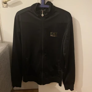 Emporio Armani (EA7) kofta - En svart Emporio Armani kofta. Sparsamt använd, i mycket gott skick. Säljes pågrund av för liten storlek. Storleken på koftan är Medium (M)