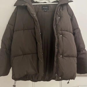 Brun dunjacka  - En brun dunjacka med luva och hög krage ifrån Monki. Köptes för 750kr Jackan är knappast använd och ser helt ny ut!