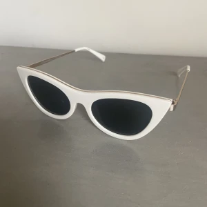 Solglasögon från Le Specs - Vita cateye solglasögon med gulddetaljer från Le Specs. Kommer i ett fodral. Solglasögonen är i nyskick men fodralet har två små fläckar som syns på nära håll. Originalpris 750 kr